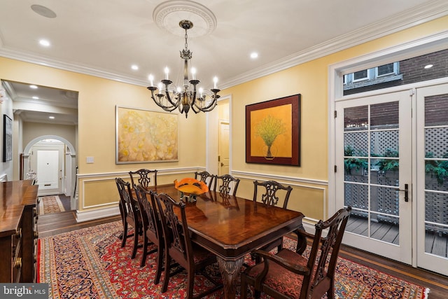 dining space with arched walkways, dark wood finished floors, wainscoting, ornamental molding, and a chandelier