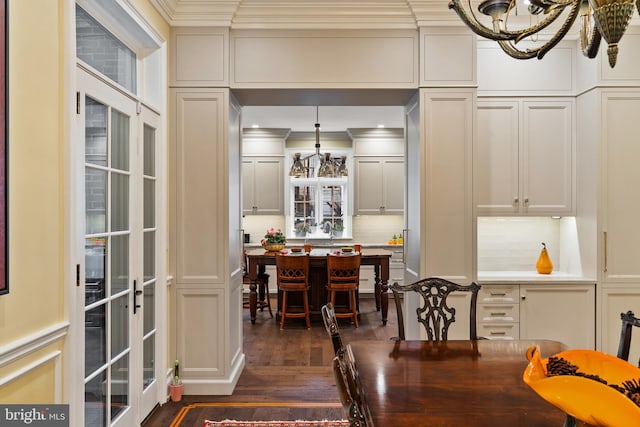 dining room featuring dark wood-style floors, french doors, a notable chandelier, a decorative wall, and ornamental molding