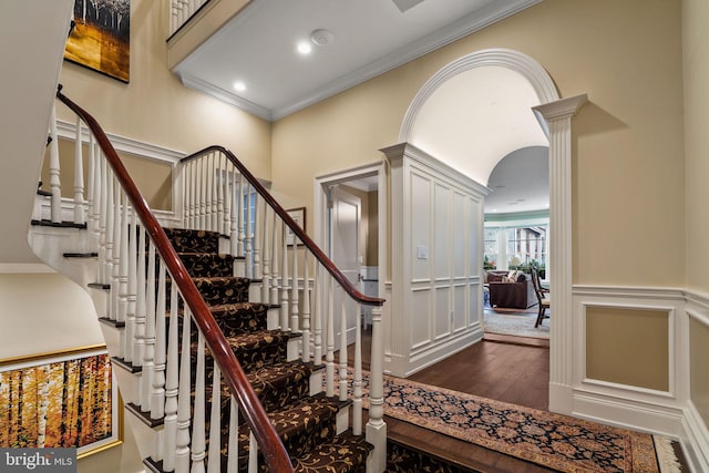 stairway with arched walkways, a decorative wall, ornamental molding, wood-type flooring, and ornate columns