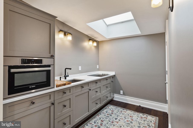 bathroom featuring a skylight, a sink, baseboards, and wood finished floors