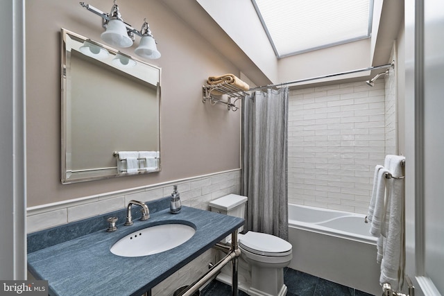 full bathroom with toilet, a wainscoted wall, a sink, tile walls, and shower / tub combo with curtain