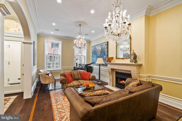 living room with a warm lit fireplace, dark wood-style floors, a chandelier, and crown molding