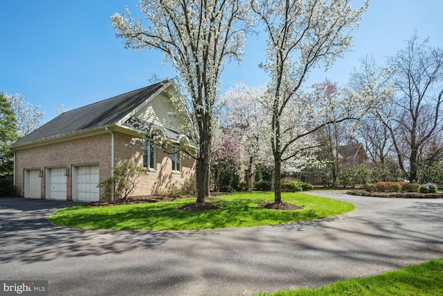 view of side of home with a garage, a lawn, brick siding, and driveway