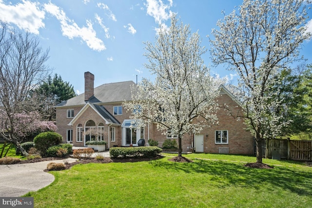 rear view of house with brick siding, a chimney, a yard, and fence