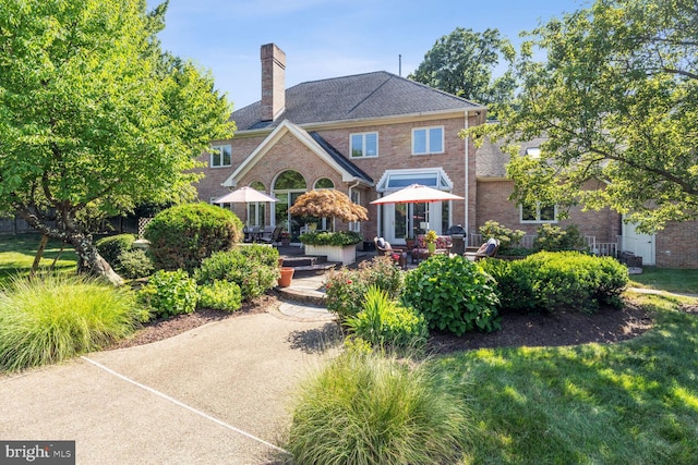 view of front of home featuring brick siding, a chimney, and a patio