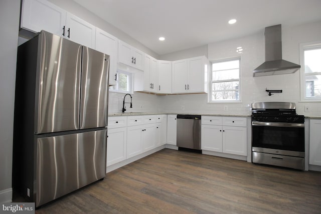 kitchen featuring sink, wall chimney exhaust hood, dark hardwood / wood-style floors, appliances with stainless steel finishes, and white cabinetry