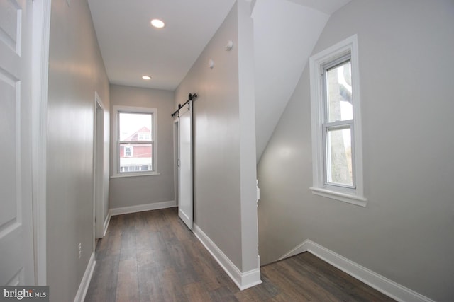 hallway with a barn door, dark hardwood / wood-style floors, and lofted ceiling