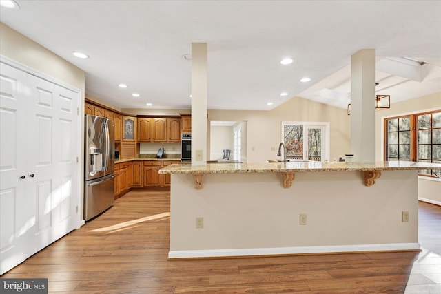 kitchen with a breakfast bar, oven, stainless steel refrigerator with ice dispenser, light stone countertops, and a wealth of natural light