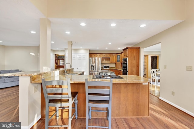 kitchen with a kitchen bar, sink, stainless steel appliances, and light hardwood / wood-style floors