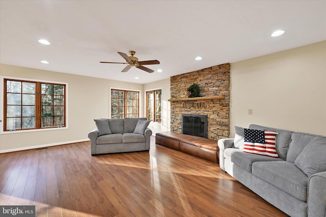 living room featuring ceiling fan, a stone fireplace, and wood-type flooring