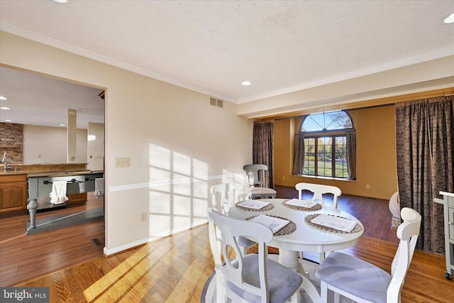 dining area with wood-type flooring, a textured ceiling, ornamental molding, and sink