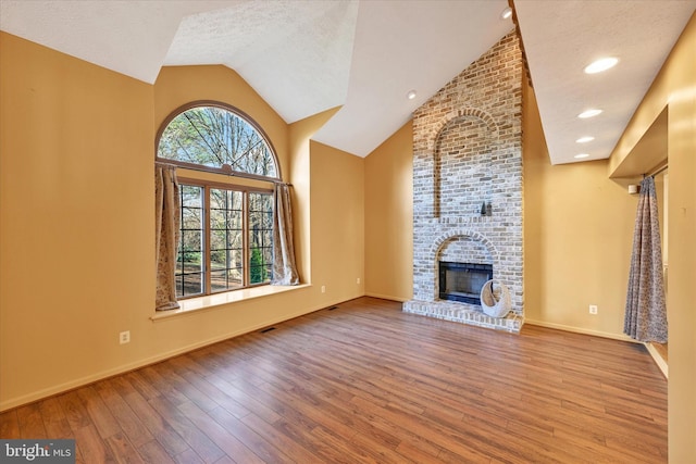 unfurnished living room with hardwood / wood-style flooring, vaulted ceiling, a fireplace, and a textured ceiling