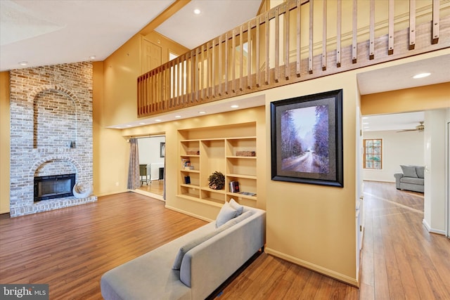 living room featuring high vaulted ceiling, hardwood / wood-style flooring, a brick fireplace, and ceiling fan