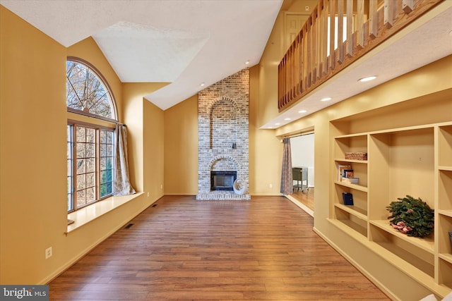 living room with hardwood / wood-style flooring, built in features, a fireplace, and high vaulted ceiling