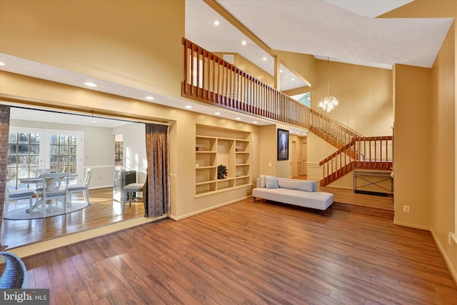 unfurnished living room featuring a notable chandelier, wood-type flooring, built in features, and a high ceiling