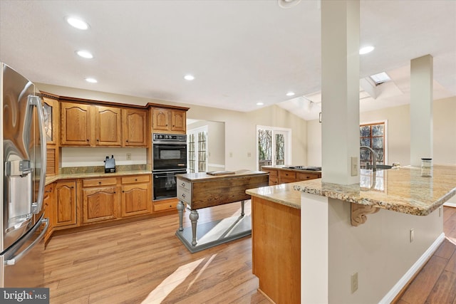 kitchen featuring light stone counters, an island with sink, stainless steel appliances, and light wood-type flooring