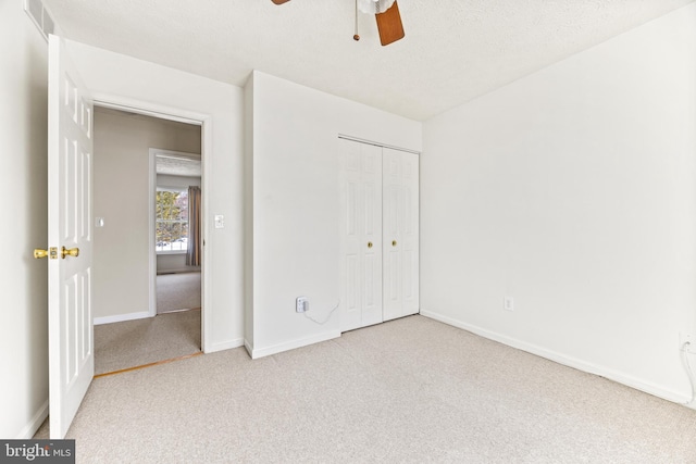 unfurnished bedroom with a textured ceiling, ceiling fan, light carpet, and a closet