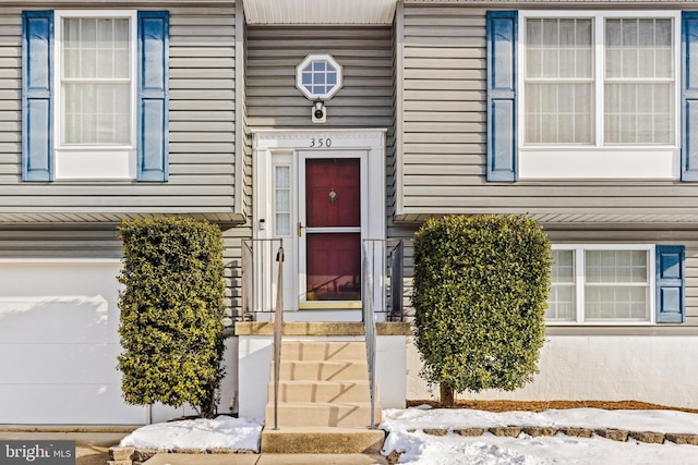 snow covered property entrance with a garage