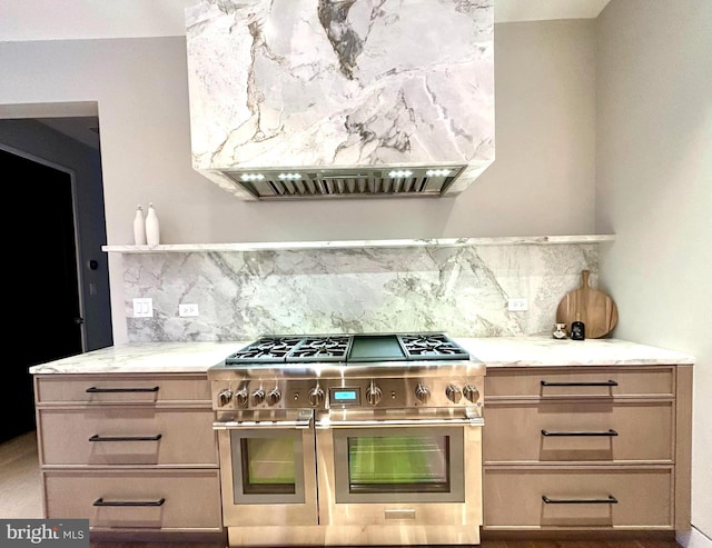 kitchen with premium range hood, light brown cabinetry, light stone counters, range with two ovens, and backsplash