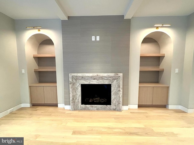 unfurnished living room featuring light hardwood / wood-style floors, a high end fireplace, and built in shelves