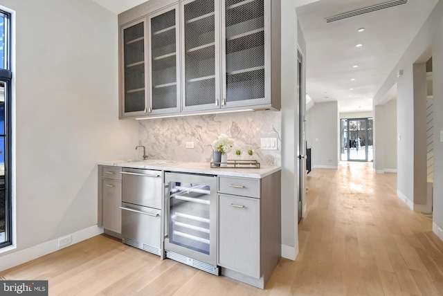 bar with tasteful backsplash, beverage cooler, light stone countertops, and light hardwood / wood-style flooring