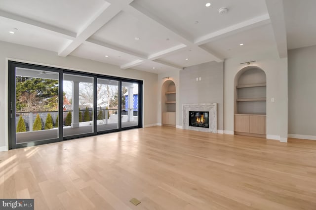 unfurnished living room with beamed ceiling, a premium fireplace, built in features, and light wood-type flooring