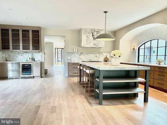 kitchen with a wealth of natural light, pendant lighting, tasteful backsplash, beverage cooler, and light hardwood / wood-style flooring