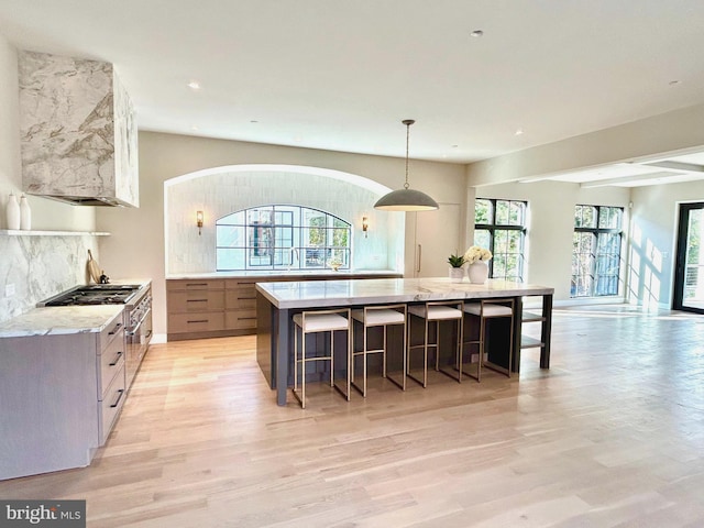 kitchen with a breakfast bar area, light stone counters, decorative backsplash, stainless steel gas cooktop, and decorative light fixtures