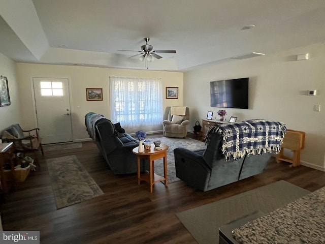 living room with a raised ceiling, ceiling fan, and dark wood-type flooring