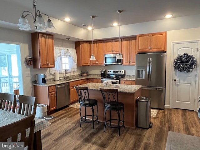 kitchen featuring pendant lighting, a center island, light stone countertops, appliances with stainless steel finishes, and a notable chandelier