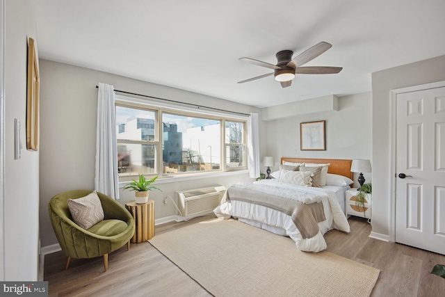 bedroom with a wall mounted AC, light hardwood / wood-style floors, and ceiling fan