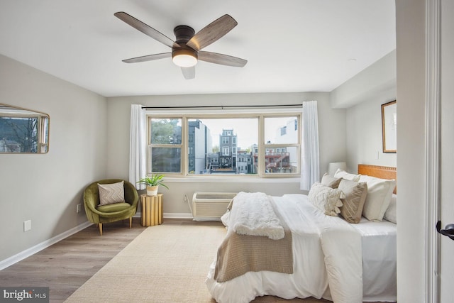 bedroom featuring a wall mounted air conditioner, ceiling fan, and light hardwood / wood-style flooring