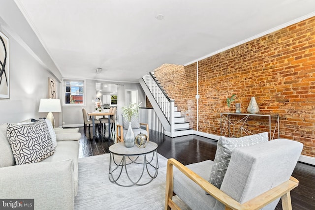 living room featuring wood-type flooring, crown molding, and brick wall