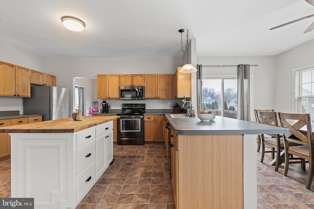 kitchen featuring pendant lighting, appliances with stainless steel finishes, butcher block counters, sink, and a kitchen island with sink