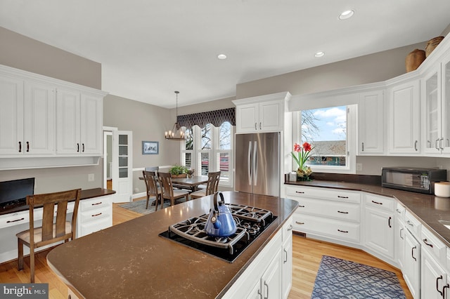 kitchen featuring black gas stovetop, pendant lighting, an inviting chandelier, white cabinets, and stainless steel fridge