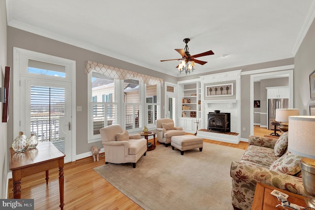 living room with ceiling fan, a wood stove, light hardwood / wood-style flooring, and crown molding