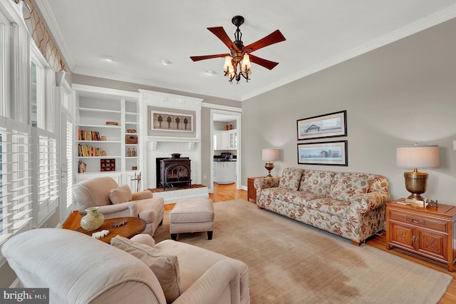 living room featuring ceiling fan, a wood stove, light hardwood / wood-style flooring, and crown molding