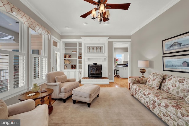 living room with light hardwood / wood-style floors, a wood stove, crown molding, and ceiling fan