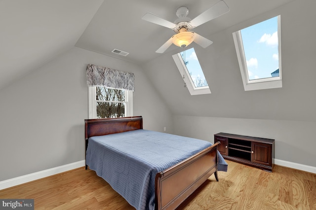 bedroom featuring ceiling fan, light wood-type flooring, and vaulted ceiling with skylight