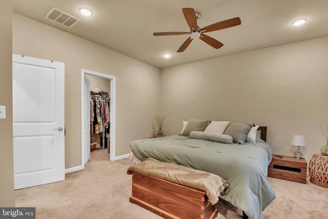 bedroom featuring ceiling fan, a walk in closet, light carpet, and a closet