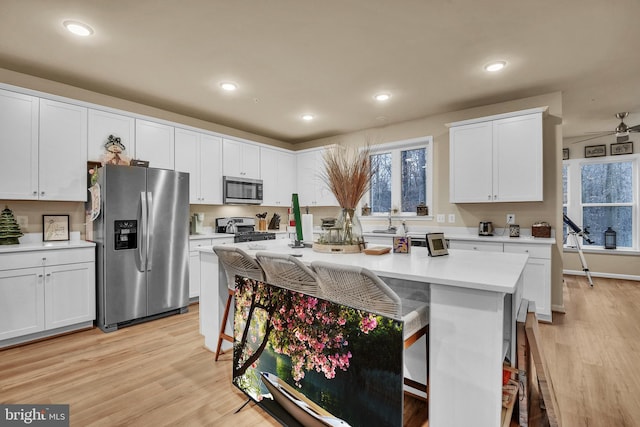 kitchen with a breakfast bar, white cabinets, ceiling fan, appliances with stainless steel finishes, and a kitchen island