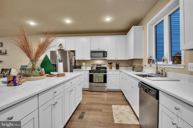 kitchen with sink, light hardwood / wood-style flooring, white cabinets, and appliances with stainless steel finishes