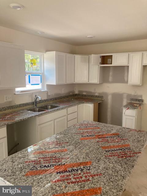 kitchen with white cabinetry, light stone counters, and sink