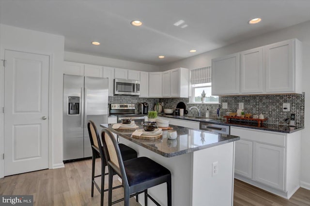 kitchen with a center island, dark stone counters, sink, appliances with stainless steel finishes, and white cabinetry