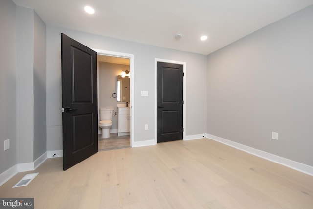 unfurnished bedroom with connected bathroom and light wood-type flooring