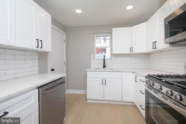 kitchen featuring sink, tasteful backsplash, light stone counters, white cabinets, and appliances with stainless steel finishes