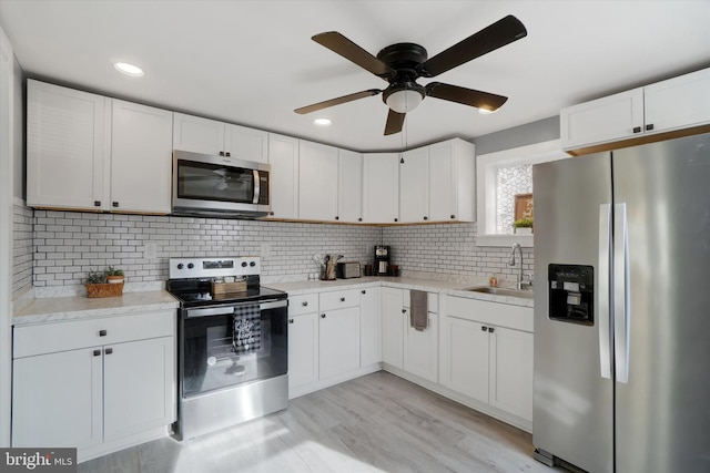 kitchen with sink, white cabinetry, tasteful backsplash, appliances with stainless steel finishes, and light hardwood / wood-style floors