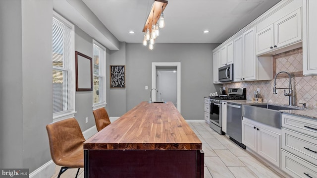 kitchen with sink, light stone countertops, decorative light fixtures, white cabinetry, and stainless steel appliances