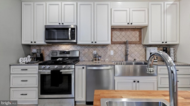 kitchen with decorative backsplash, light stone counters, stainless steel appliances, sink, and white cabinetry