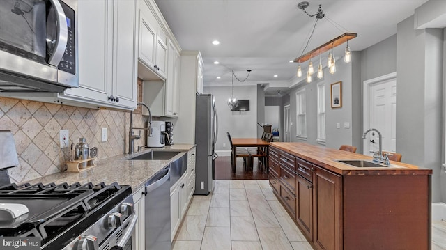 kitchen with sink, hanging light fixtures, stainless steel appliances, wood counters, and white cabinets